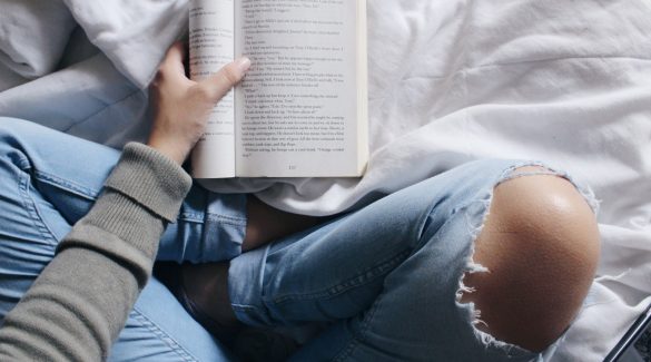 Adolescente dans un jean trouvé qui lit un livre sur son lit à côté de son smartphone