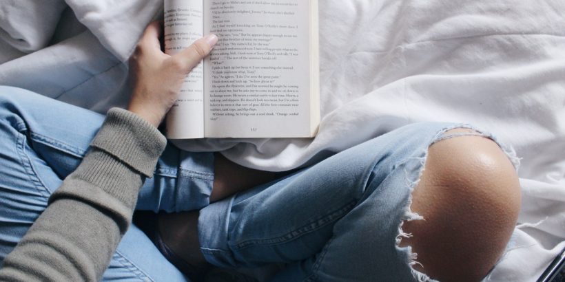 Adolescente dans un jean trouvé qui lit un livre sur son lit à côté de son smartphone