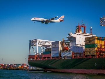 bateau avec conteneurs et avion qui passe au-dessus