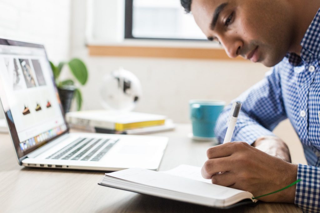 homme qui prend des notes devant un ordinateur portable